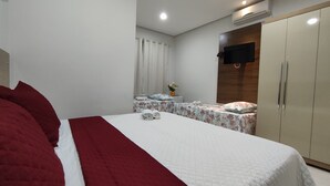 Una habitación de hotel con una cama grande, un armario, un escritorio con silla, un televisor montado en la pared y un equipo de aire acondicionado.