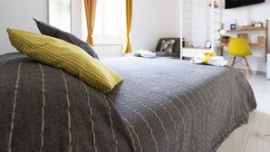 Een netjes opgemaakt bed met gestreept beddengoed, een televisie aan de muur en een bureau met een stoel op de achtergrond.