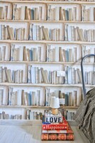 A bookshelf filled with books, a lamp on a table, and a blanket on a couch.