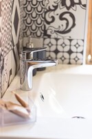 Un baño con un grifo moderno, dispensador de jabón y baldosas decorativas en la pared.