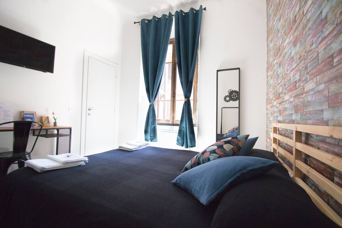 A bedroom with a bed, a desk, a chair, and a window with curtains.