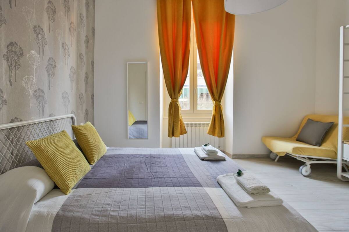 A hotel room with a bed, a bedside table, a chair, and a window with curtains.