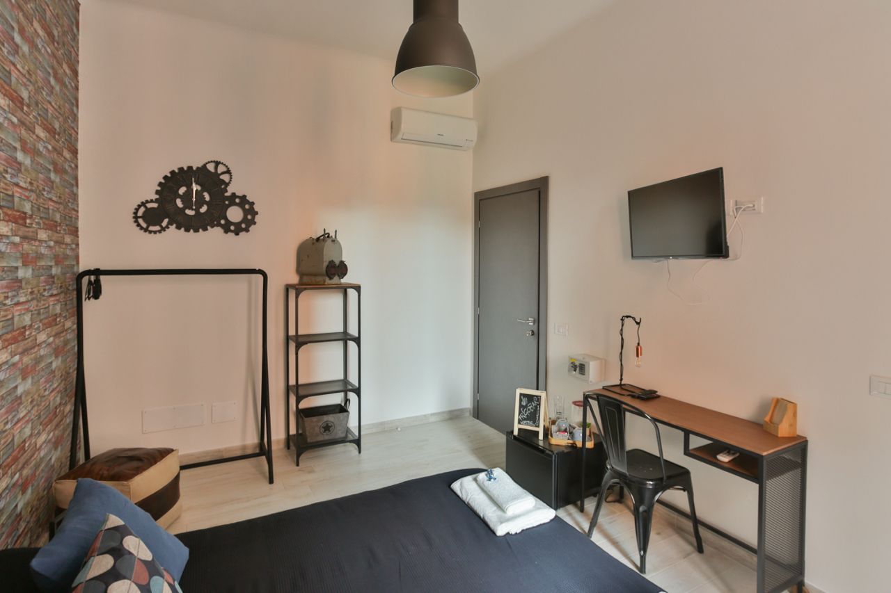 Een slaapkamer met een bed, een bureau, een stoel, een televisie en een wandplank.