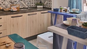 Een moderne keuken met houten kastjes, een decoratieve spatwand en een eethoek met een blauwe tafel en witte stoelen.