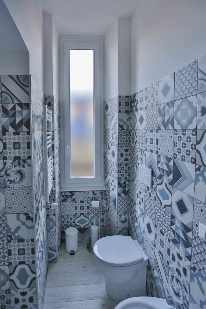 Une salle de bain avec des carreaux décorés, des toilettes, un bidet et une fenêtre.