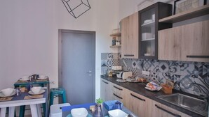 Een compacte keuken met moderne kastinrichting, een eethoek met een tafel voor twee personen, en diverse keukenapparaten en keukengerei.
