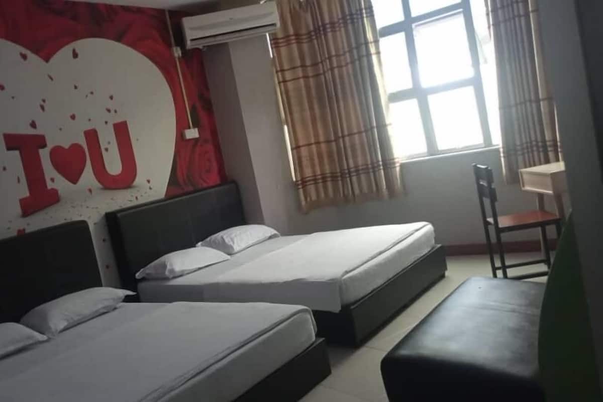Habitación de hotel con dos camas, una decoración grande en forma de corazón en la pared y una ventana con cortinas.