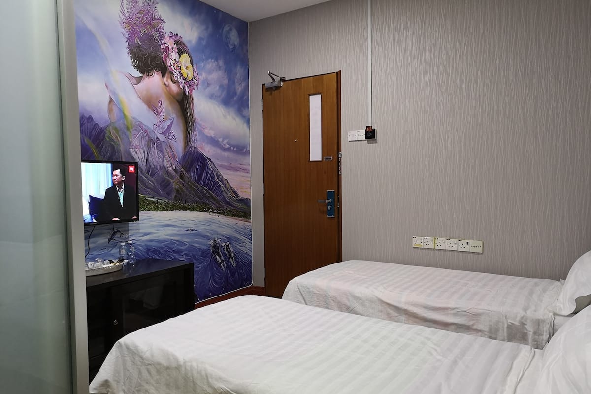 Habitación de hotel con dos camas, un televisor sobre un mueble, un mural en la pared y una puerta de madera.