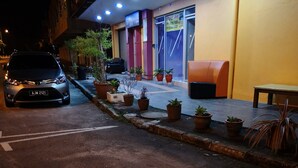 A building with a parking area, potted plants, and a seating area with a bench and a table. - Home Inn (Ipoh)