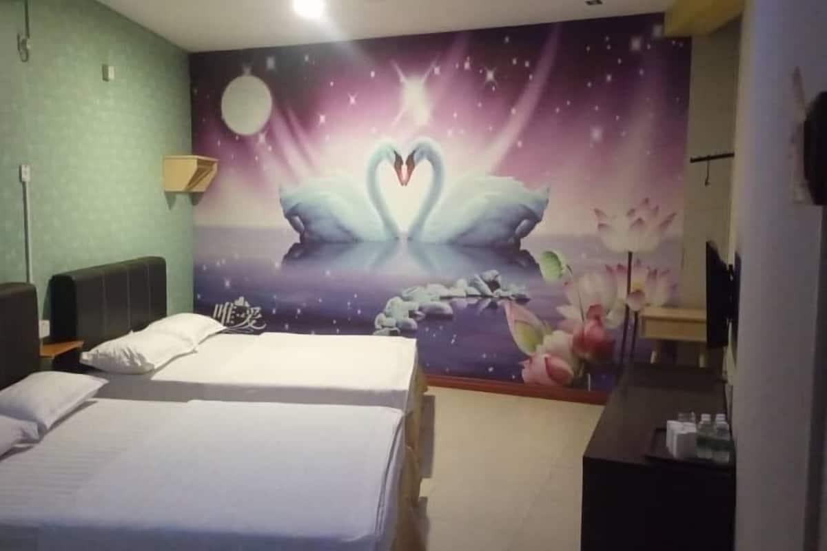 Habitación de hotel con cama, mesita de noche, lámpara de pared y un mural decorativo con cisnes y un corazón.