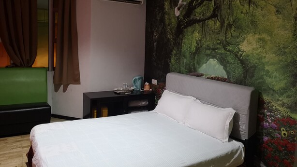 A bedroom with a bed, a nightstand, a green couch, and a forest-themed wall mural. - Home Inn (Ipoh)