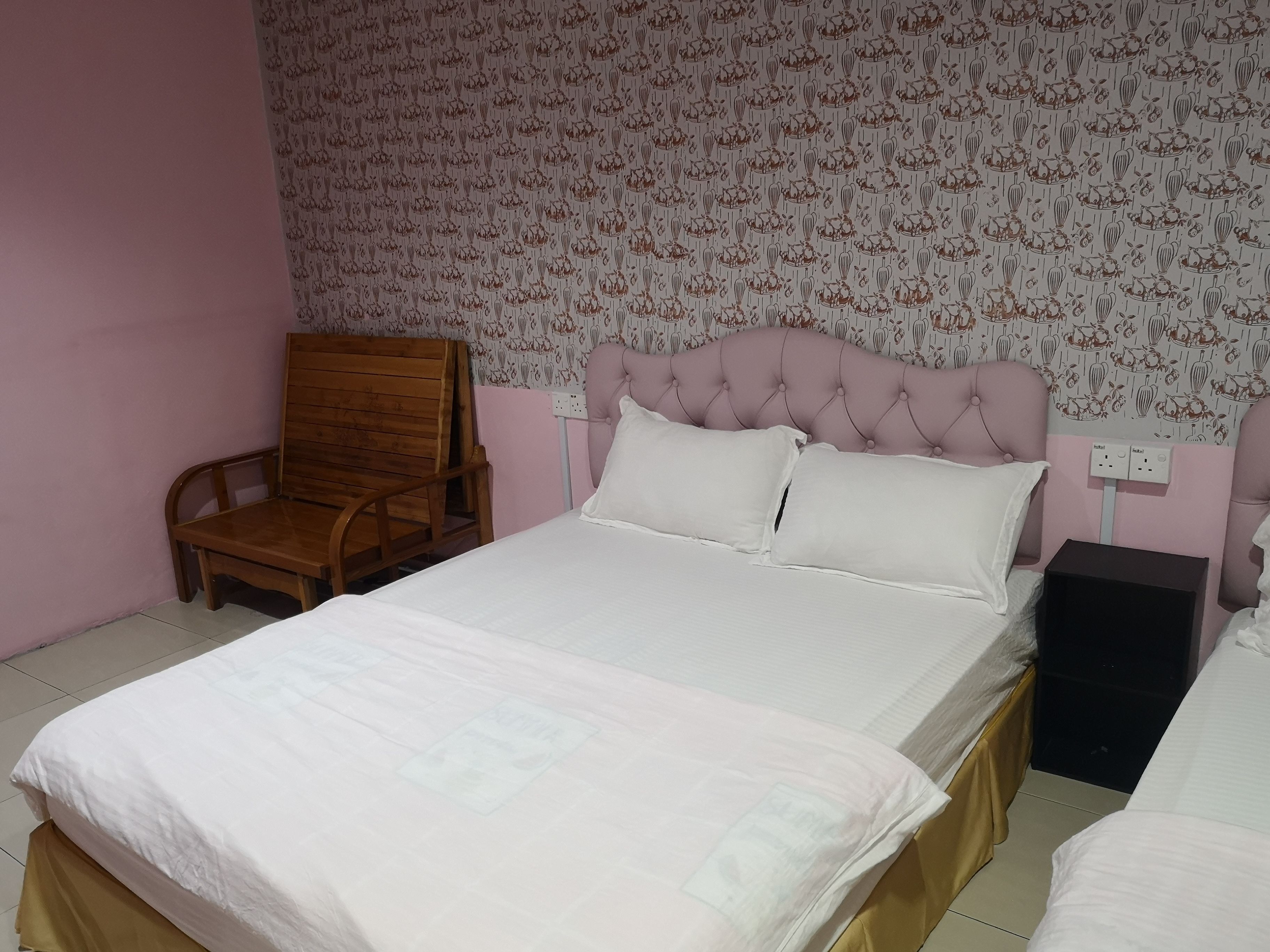 A bedroom with a bed, a wooden chair, a bedside table, and a power outlet on the wall.