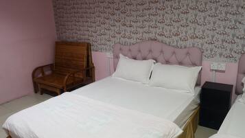 A bedroom with a bed, a wooden chair, a bedside table, and a power outlet on the wall.