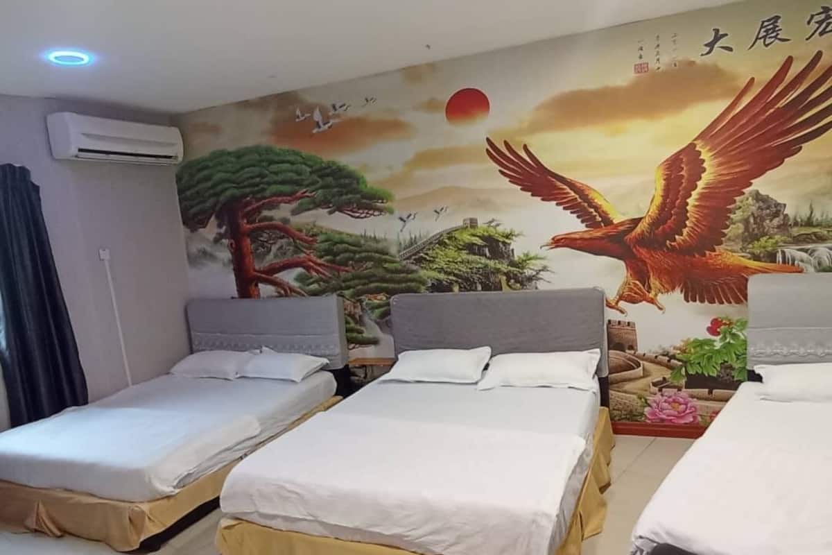 Habitación de hotel con tres camas individuales, un mural con un pájaro y un árbol, y un equipo de aire acondicionado.