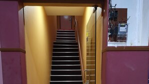 A staircase leading to an upper floor, flanked by walls painted in yellow and purple, with potted plants at the bottom. - Home Inn (Ipoh)