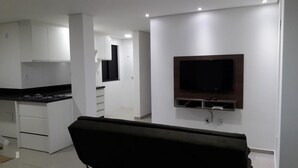 Een moderne keuken met witte kasten, een zwart aanrecht en een ingebouwde kookplaat. Er hangt een flatscreen televisie aan de muur boven een houten plank.