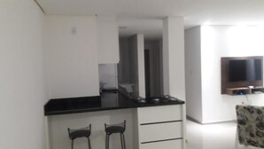 Een kleine keuken met een zwart aanrecht, twee barkrukken, een inbouwfornuis en een televisie aan de muur.