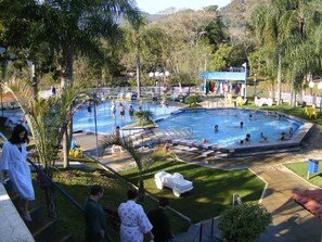 Un espace piscine comprenant plusieurs piscines, des chaises longues et un coin salon abrité.