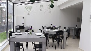 Un espace de restauration moderne, doté de plusieurs tables et chaises, de grandes fenêtres donnant sur la rue et d’œuvres d’art décoratives sur les murs.
