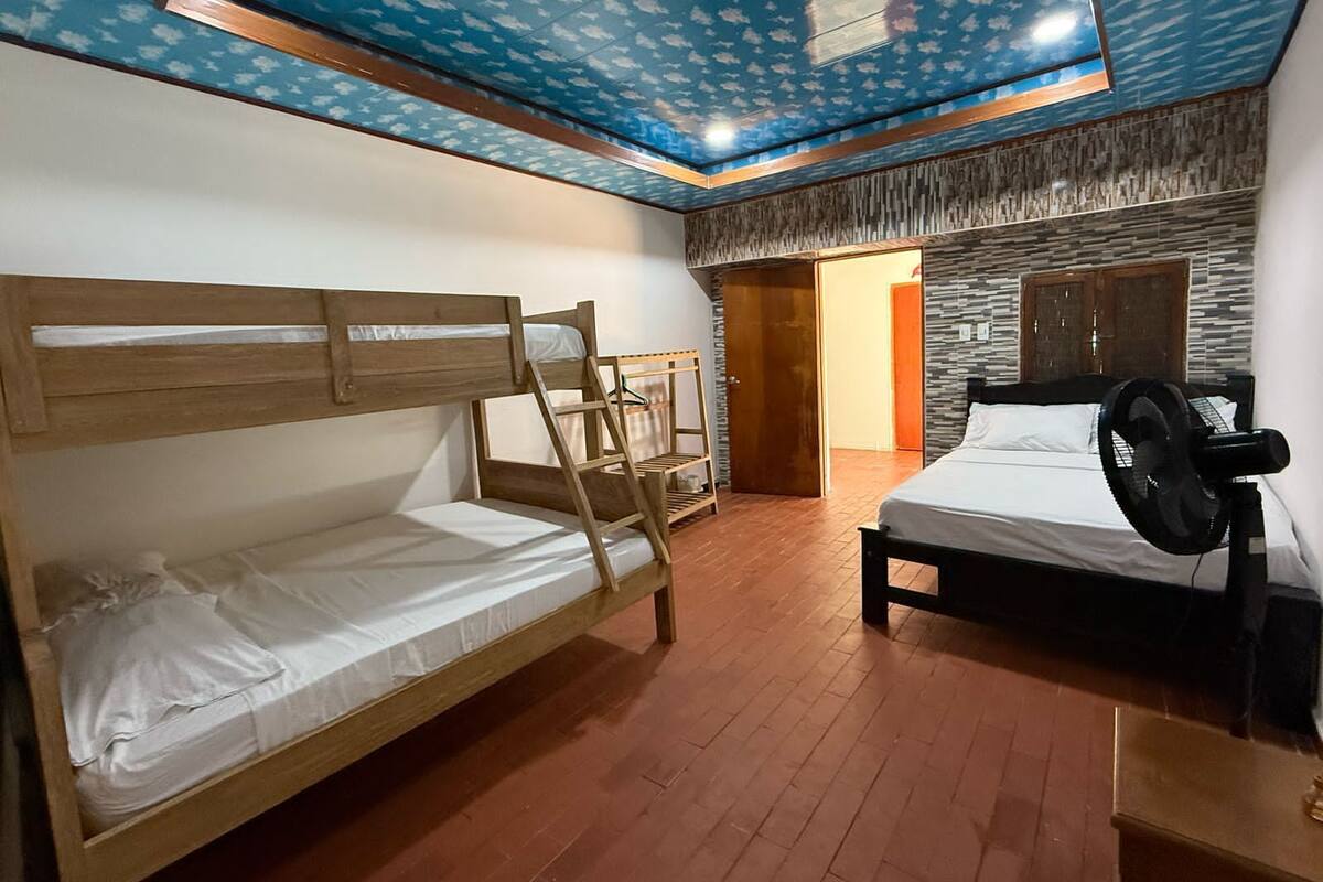 A room with bunk beds, a single bed, a fan, and a door leading to another room.