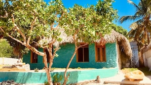 Una casa con techo de paja, un ventanal pequeño y un árbol en primer plano.