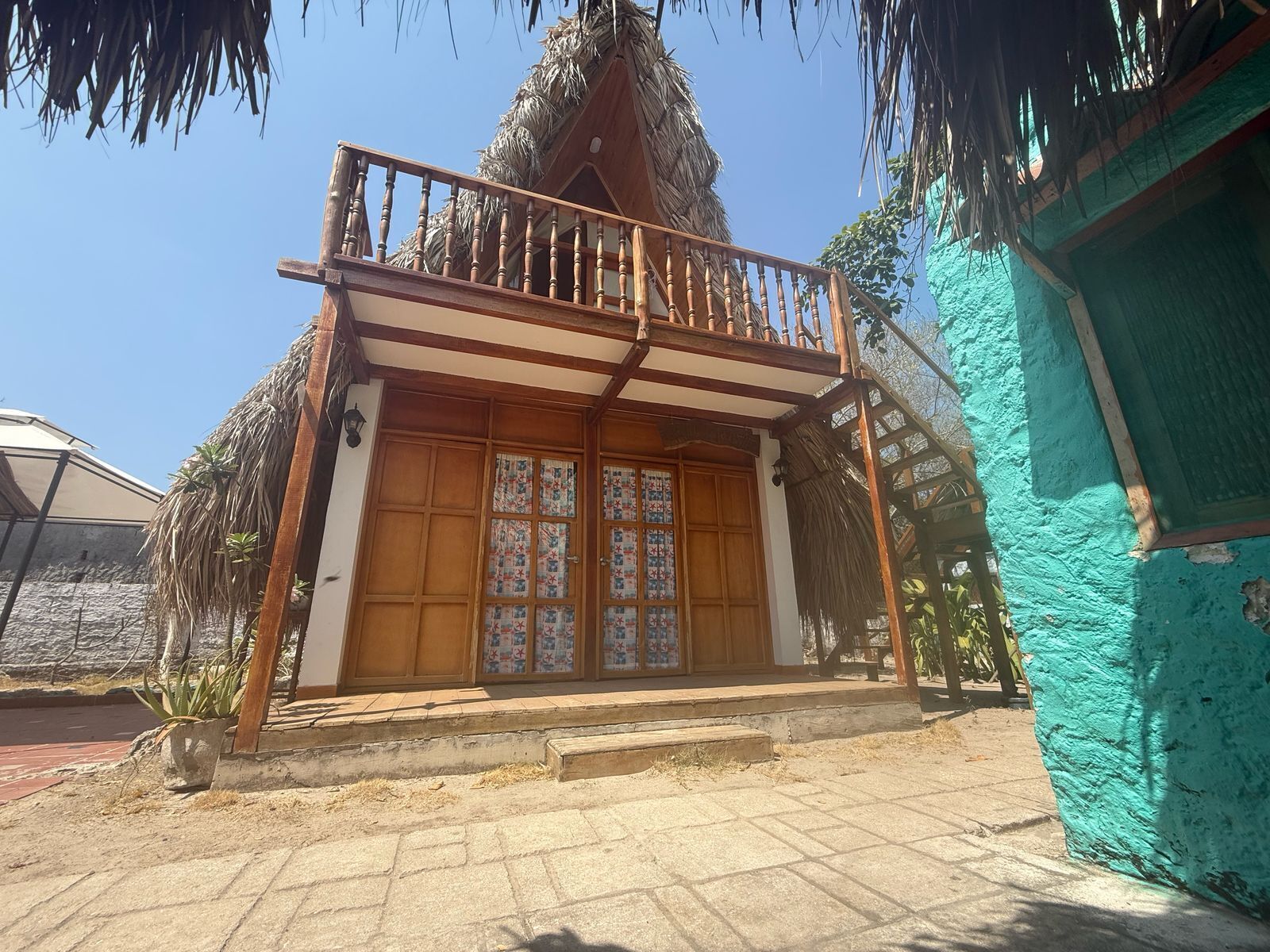 Uma casa de madeira tradicional com varanda, telhado de palha e entrada em tijolos.