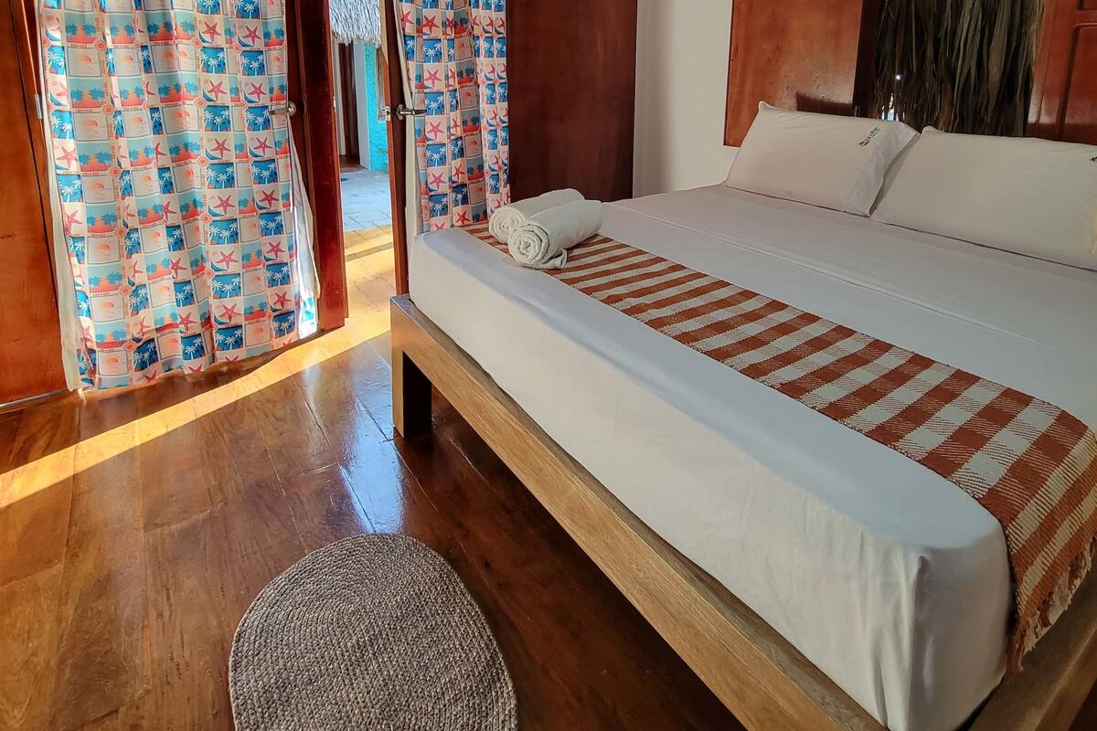 A bedroom with a wooden bed, a round rug, and a view through a door with patterned curtains.