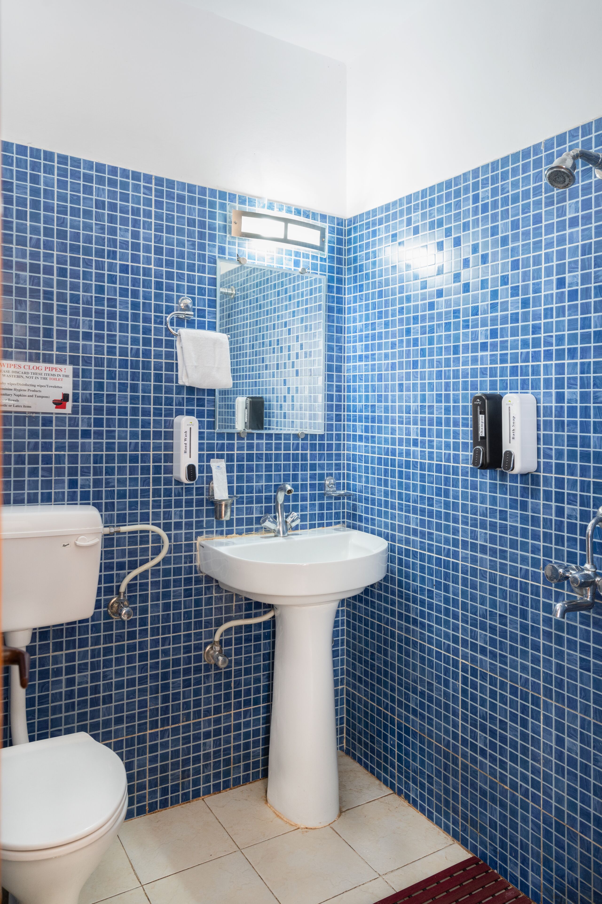 A bathroom with blue tiled walls, a white sink, a toilet, and a shower.