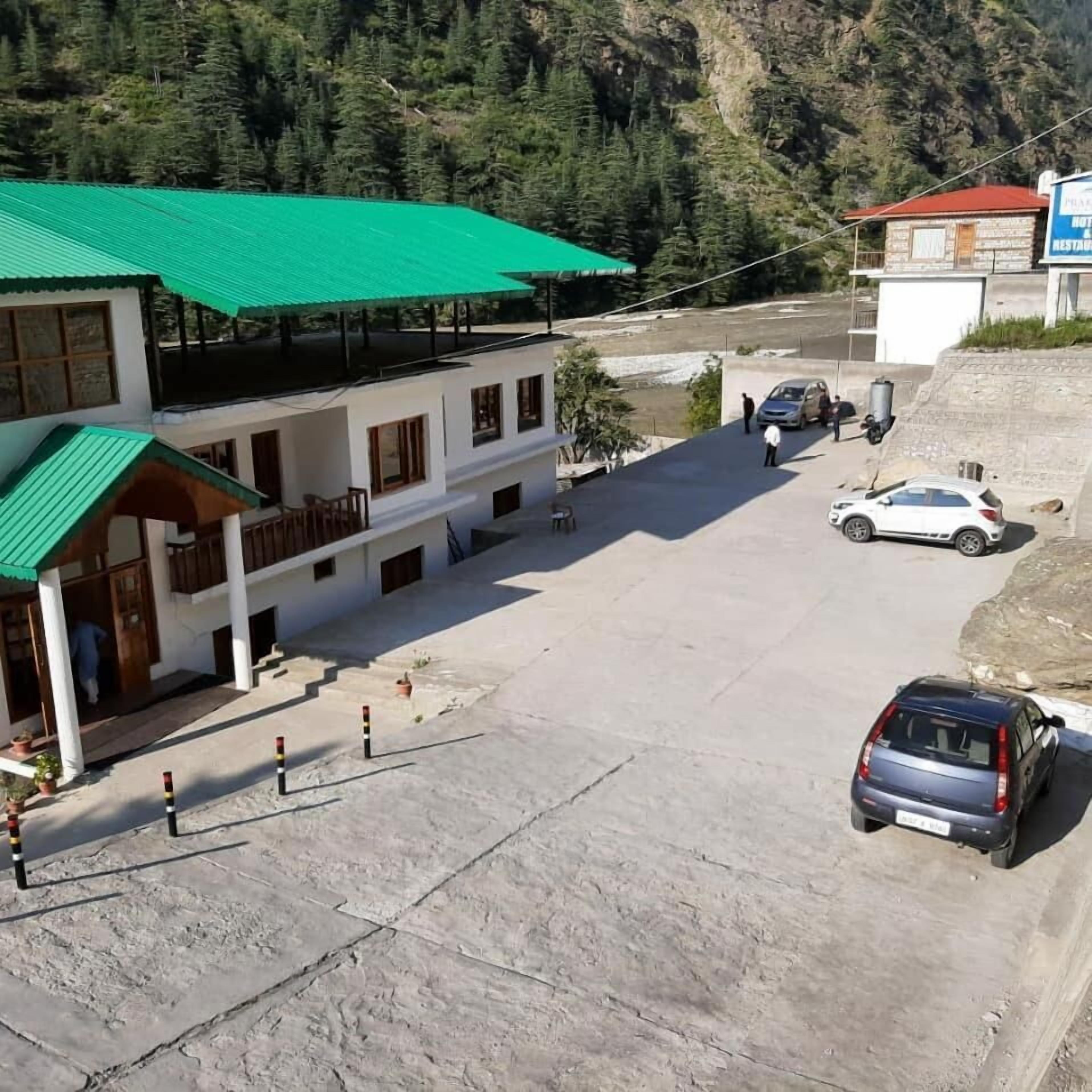 A two-story building with a green roof, a parking area, and a mountainous backdrop.