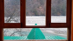 Una ventana con vista a un paisaje nevado, un río y una estructura verde en primer plano.
