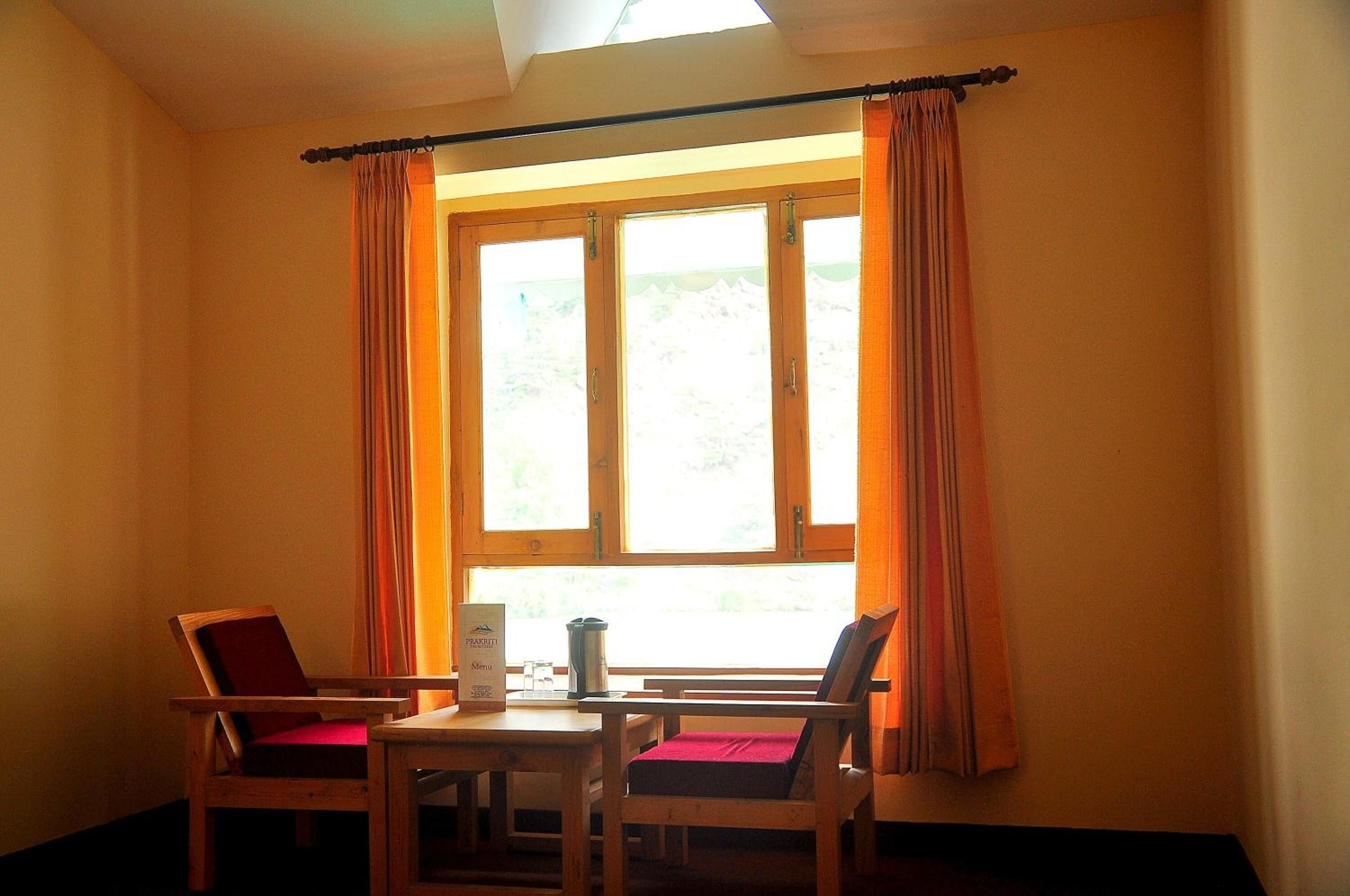 A room with a wooden table and two chairs, a window with curtains, and a sign on the table.