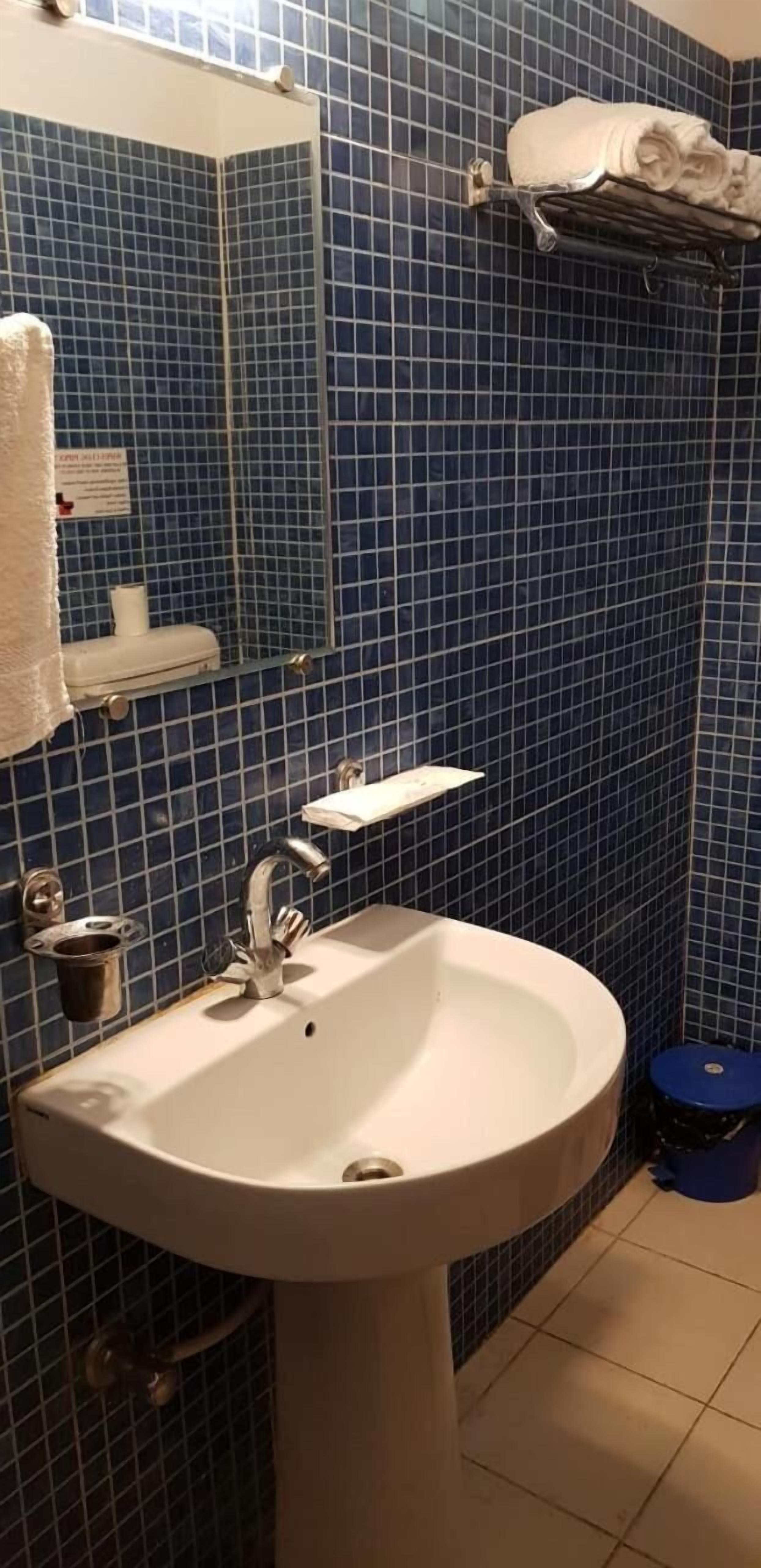 A bathroom with a white sink, blue-tiled walls, a mirror, and a towel rack.
