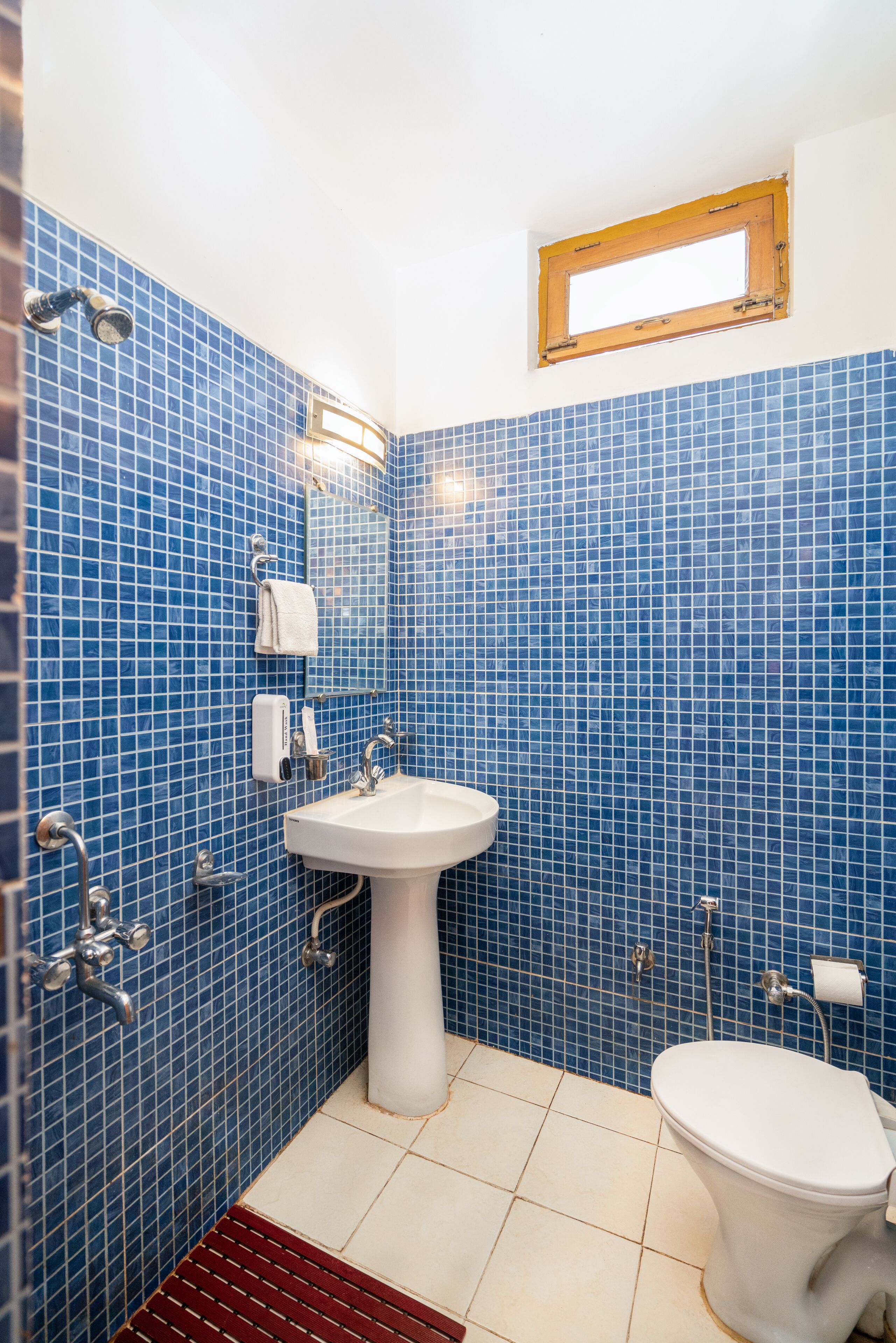 A bathroom with blue mosaic tiles, a white sink, a toilet, and a window with a wooden frame.