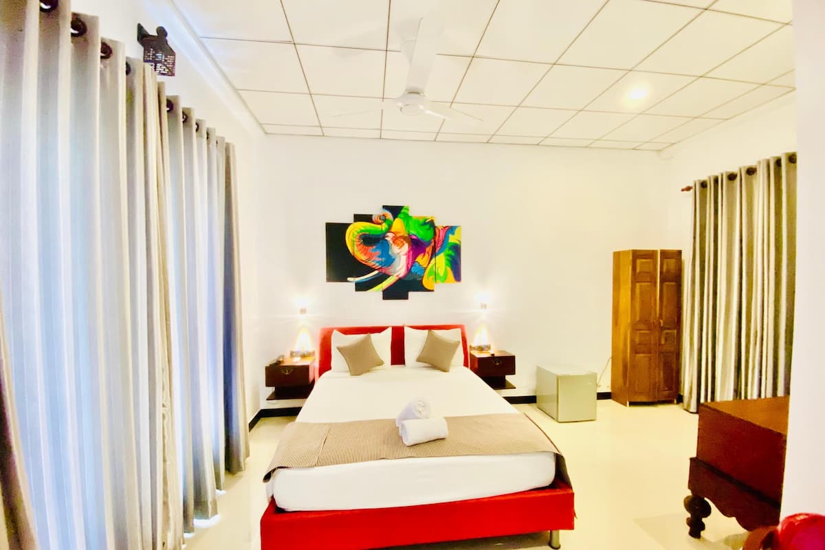 Una habitación de hotel con una cama grande, un ventilador de techo, un cuadro en la pared y un armario de madera.