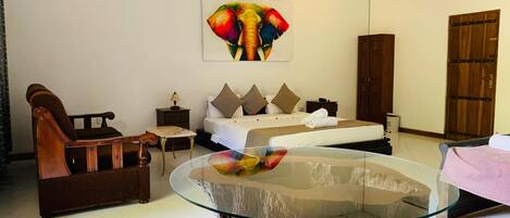 A hotel room with a bed, a wooden chair, a glass table, and a large elephant painting on the wall.
