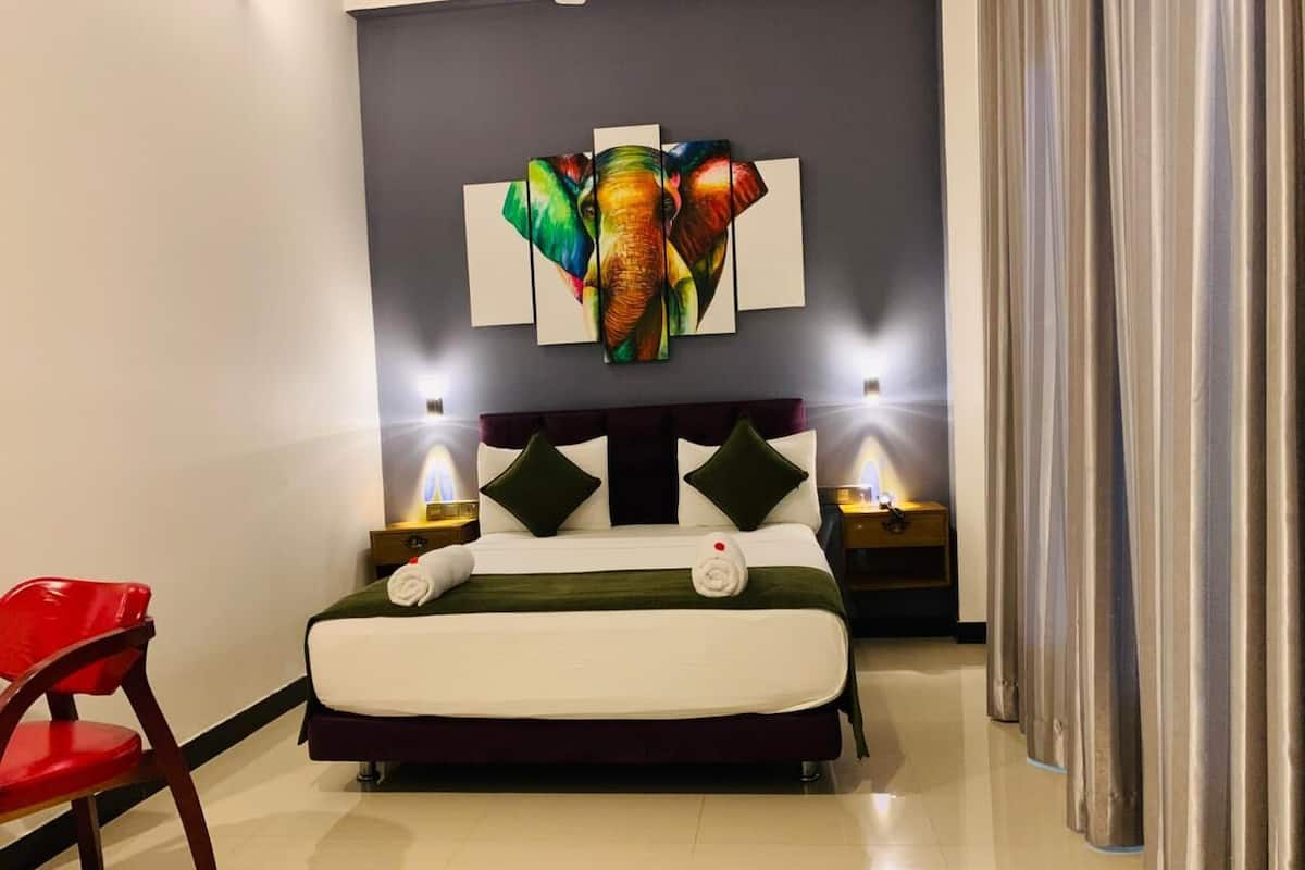 Una habitación de hotel con una cama, una silla roja, una obra de arte en la pared y dos lámparas de noche.