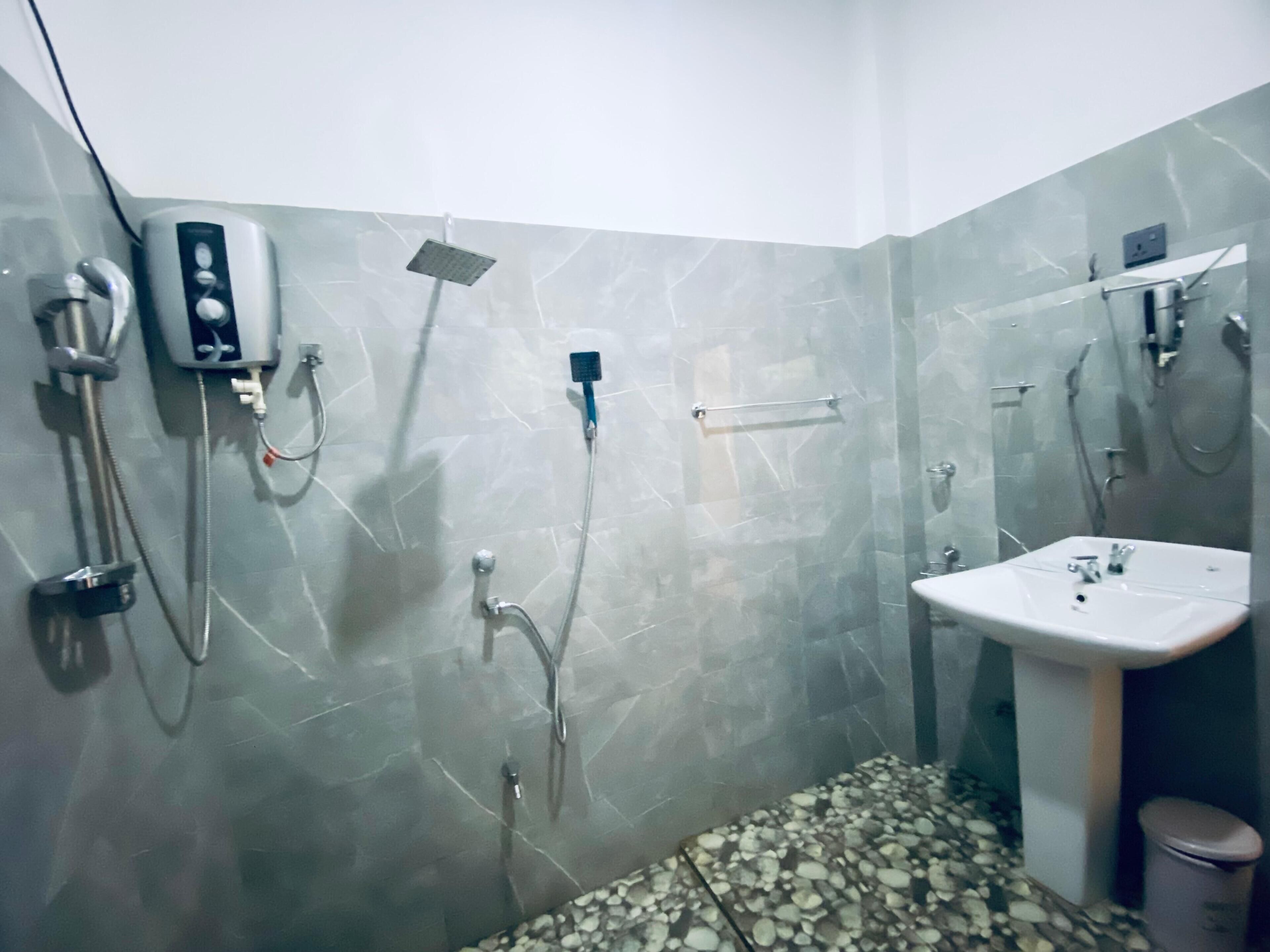 A bathroom with a marble floor, a sink, and a shower with a handheld showerhead and a wall-mounted faucet.