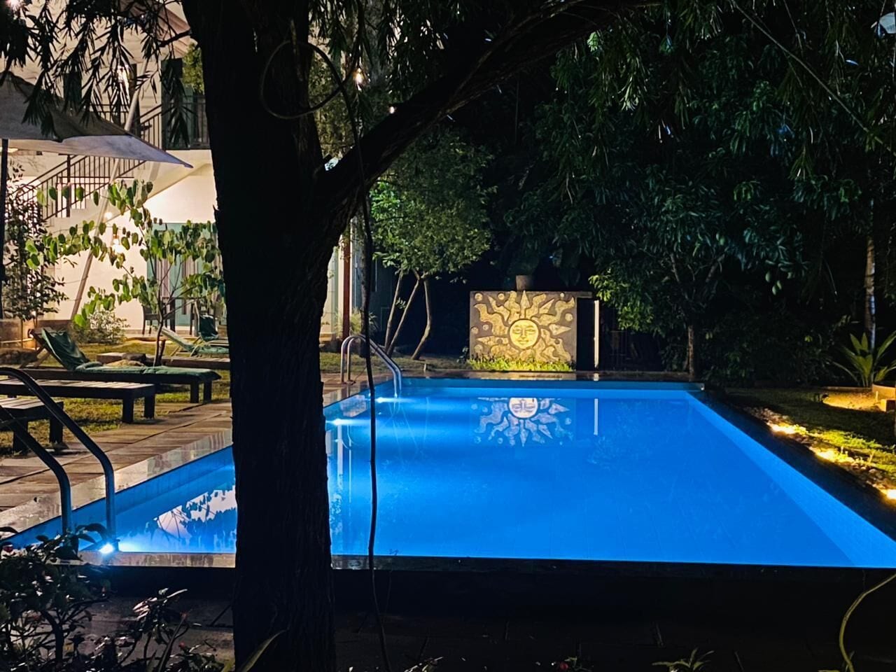 Una piscina con diseño de sol, rodeada de árboles y un área de descanso.