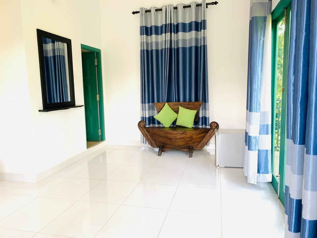 Um corredor com um banco de madeira, cortinas listradas e uma porta verde.