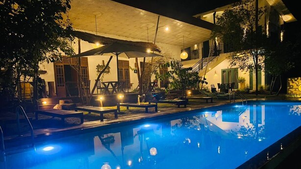 Une piscine intérieure dotée de chaises longues et de tables, entourée d’un patio couvert agrémenté de plantes et d’un escalier.