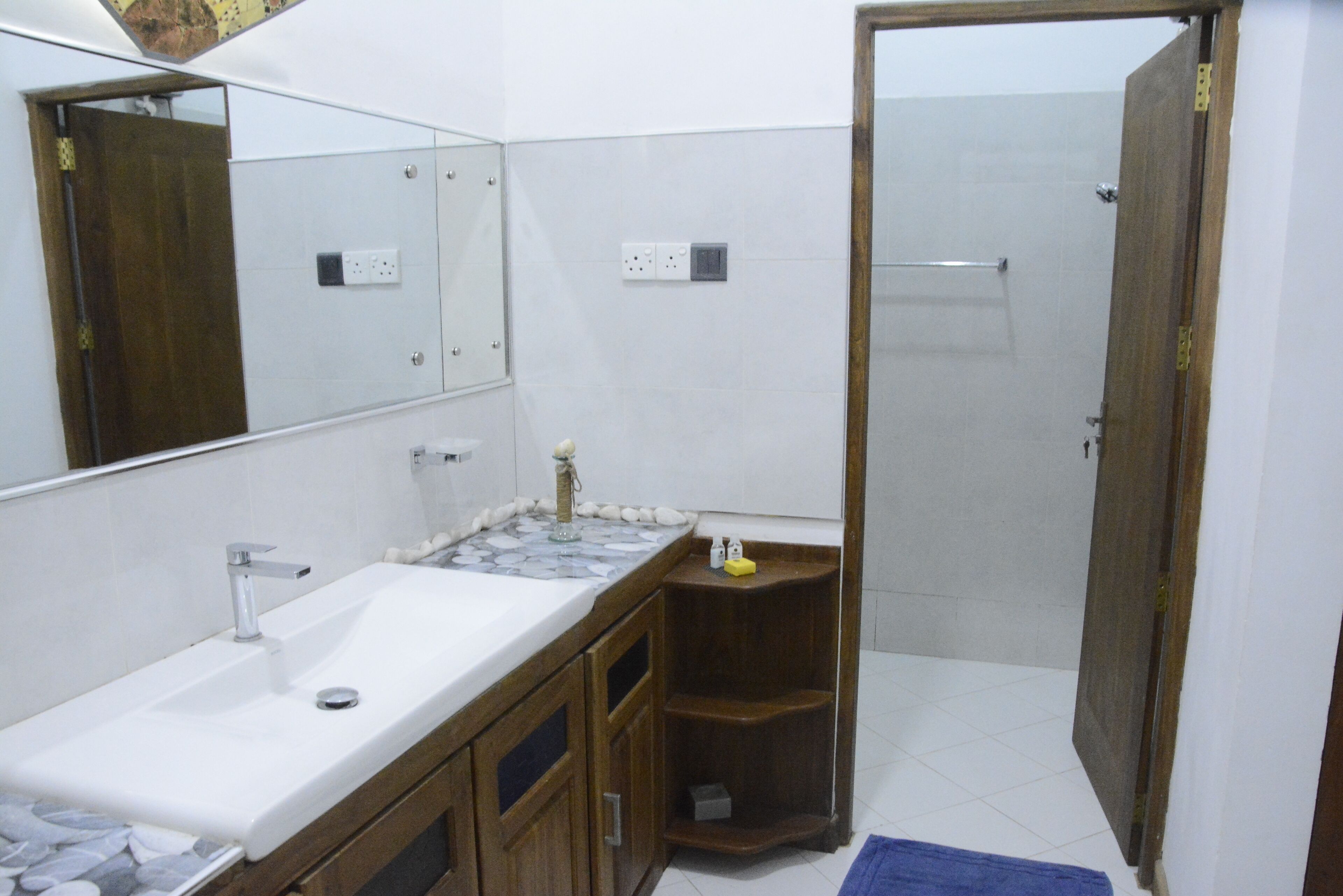 Un baño con lavamanos blanco, un espejo, un mueble de madera y una zona de ducha.