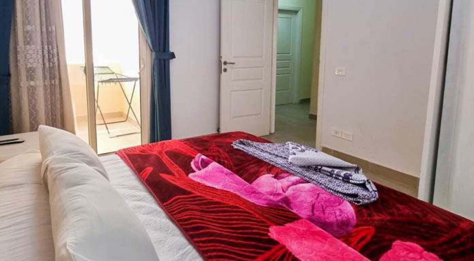 Habitación de hotel con cama, colcha estampada en rojo y negro, y ventana con cortinas.