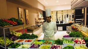 Un chef de cocina parado en una cocina con diversos vegetales expuestos frente a él.