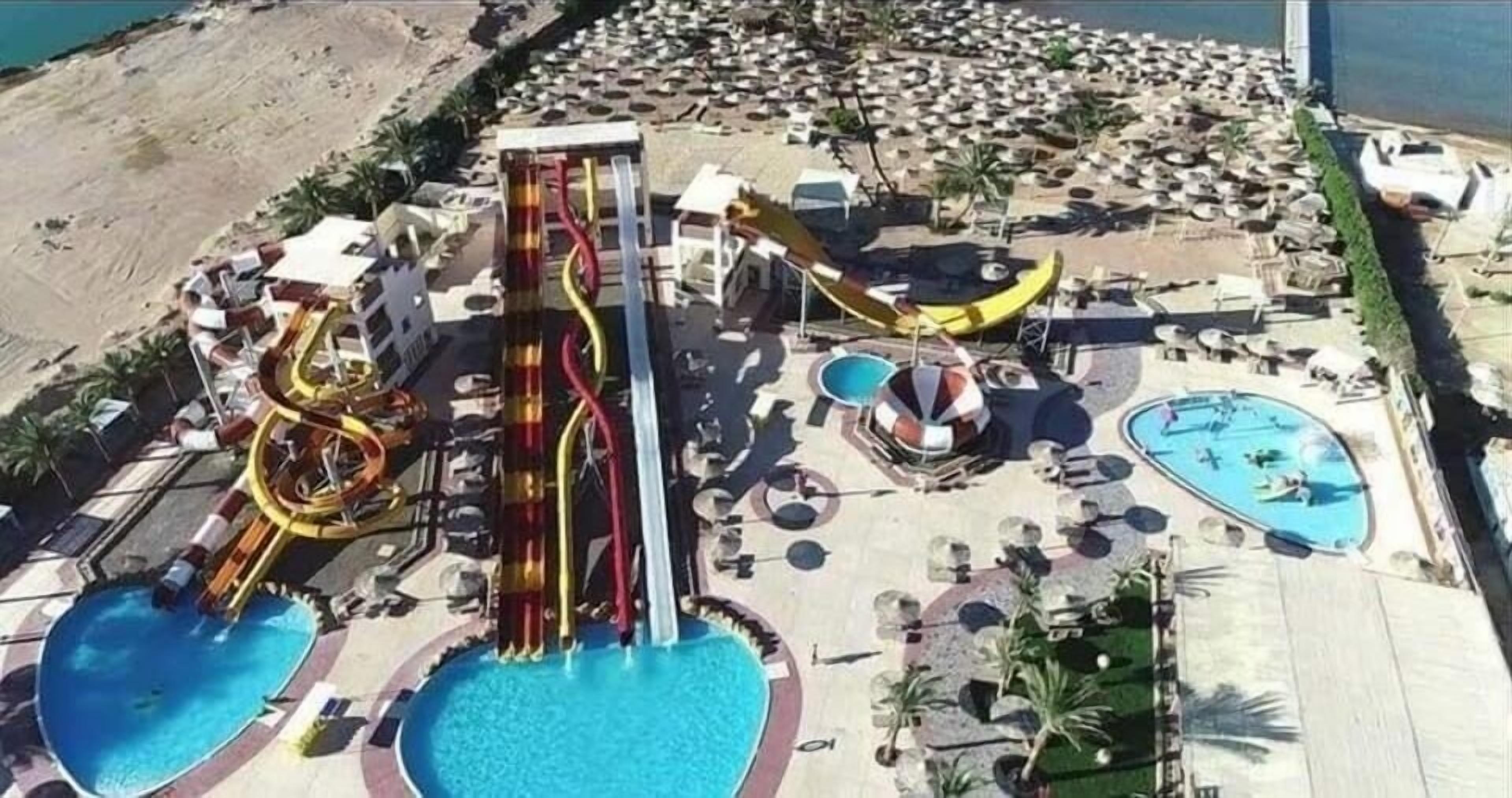 A water park with multiple slides and pools, surrounded by lounge chairs and umbrellas.