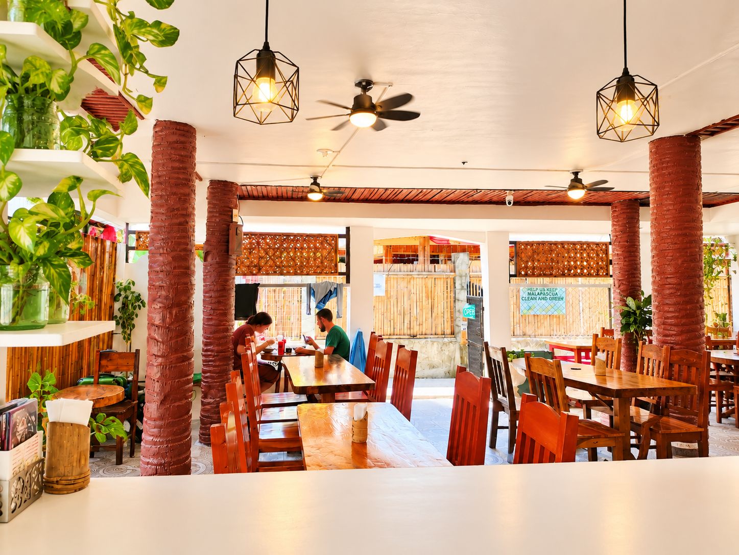 Un restaurante con mesas y sillas de madera, plantas colgantes y ventiladores de techo.