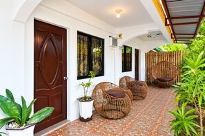 A corridor with a tiled floor, a wooden door, and wicker chairs. - Guanna's Place Room and Resto Bar (Daanbantayan)