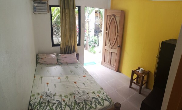 A bedroom with a bed, a wooden door, a small table, and a window with curtains. - Guanna's Place Room and Resto Bar (Daanbantayan)