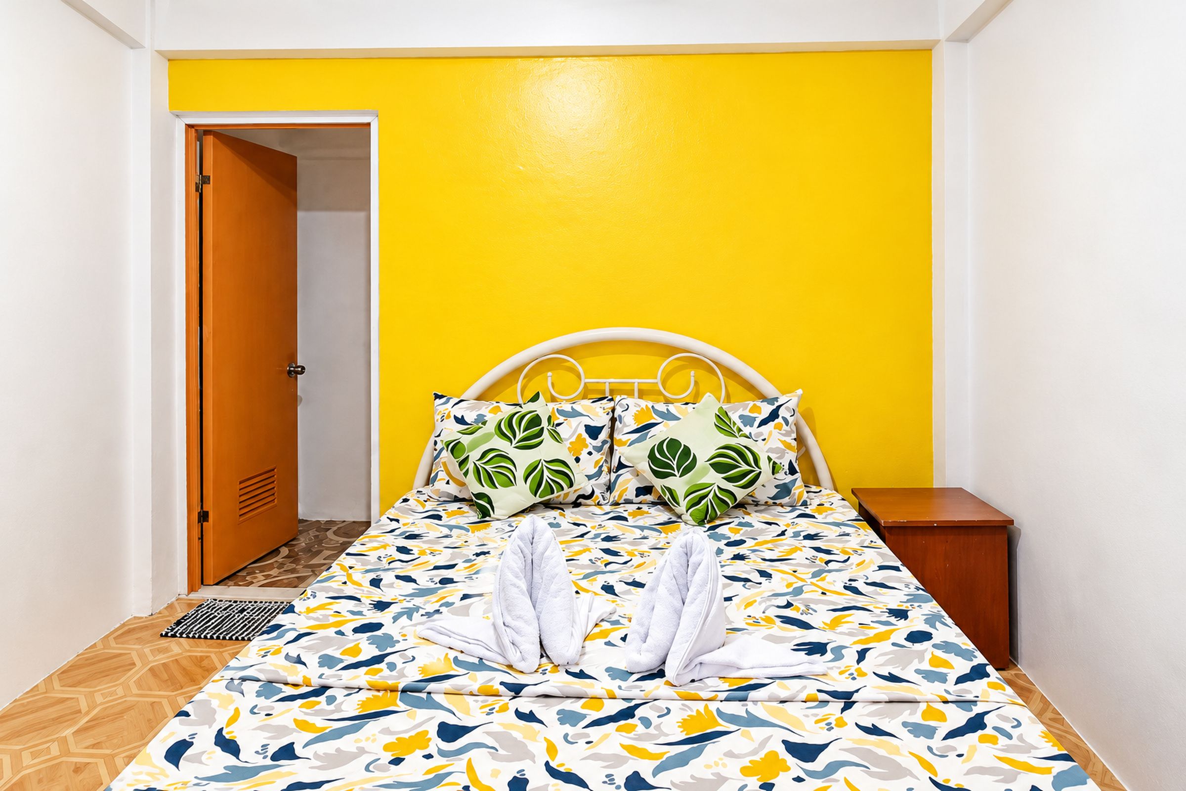 A bed with a patterned bedspread, pillows with leaf designs, and a white headboard.