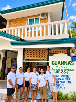 A guesthouse with a balcony, a signboard advertising services, and a group of people standing in front. - Guanna's Place Room and Resto Bar (Daanbantayan)