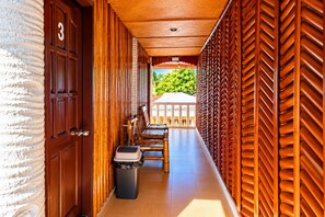 A corridor with a wooden door marked with the number 3, a trash bin, and a seating area with a view of greenery outside. - Guanna's Place Room and Resto Bar (Daanbantayan)